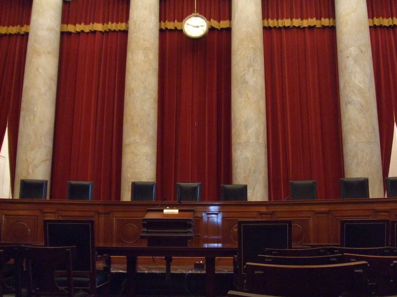 United States Supreme Court chamber with symmetrical columns, red curtains, and nine empty chairs